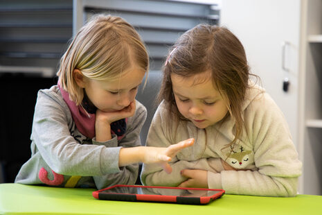 Zwei Mädchen sitzen am Tisch und schauen auf ein Tablet