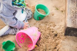 Ein Kind kniet von Eimer und Förmchen umgeben im Sandkasten