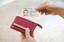 Eine Person zieht einen Personalausweis mit elektronischer Identifikation aus einer roten Geldbörse