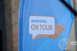 Das Bild zeigt eine blaue Fahne mit der Aufschrift "Gigabitbüro on Tour".
