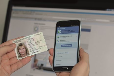 Ein Person hält einen neuen Personalausweis mit elektronischer Identifikation neben ein Smartphone mit geöffneter App