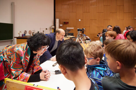 Enfants et professeurs se penchent ensemble dans l'amphithéâtre sur une table couverte de documents.