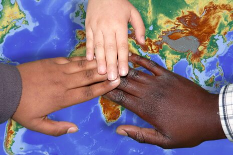 Tre persone di diverso colore della pelle tengono insieme un mappamondo tra le mani