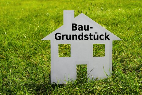 Ein Haus aus Pappe steht auf einer Wiese. Auf dem Haus steht "Baugrundstück".