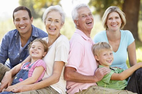 Eine sechsköpfige Familie sitzt auf einer Wiese und lacht in die Kamera.