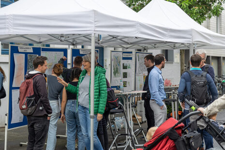 The picture shows people looking at maps at a city information stand.