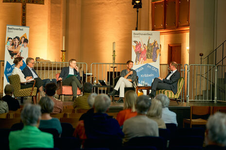 Five people sit on a stage and talk