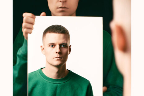 A person shows himself a photo of a man in the mirror